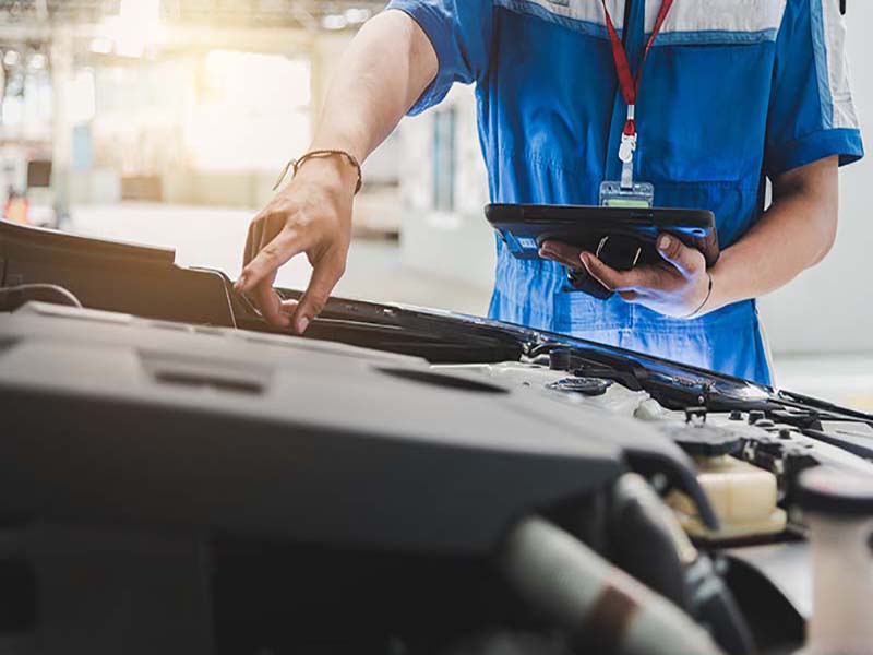 Garagiste effectuant une inspection d'un moteur d'un véhicule d'occasion en suivant un protocole électronique.
