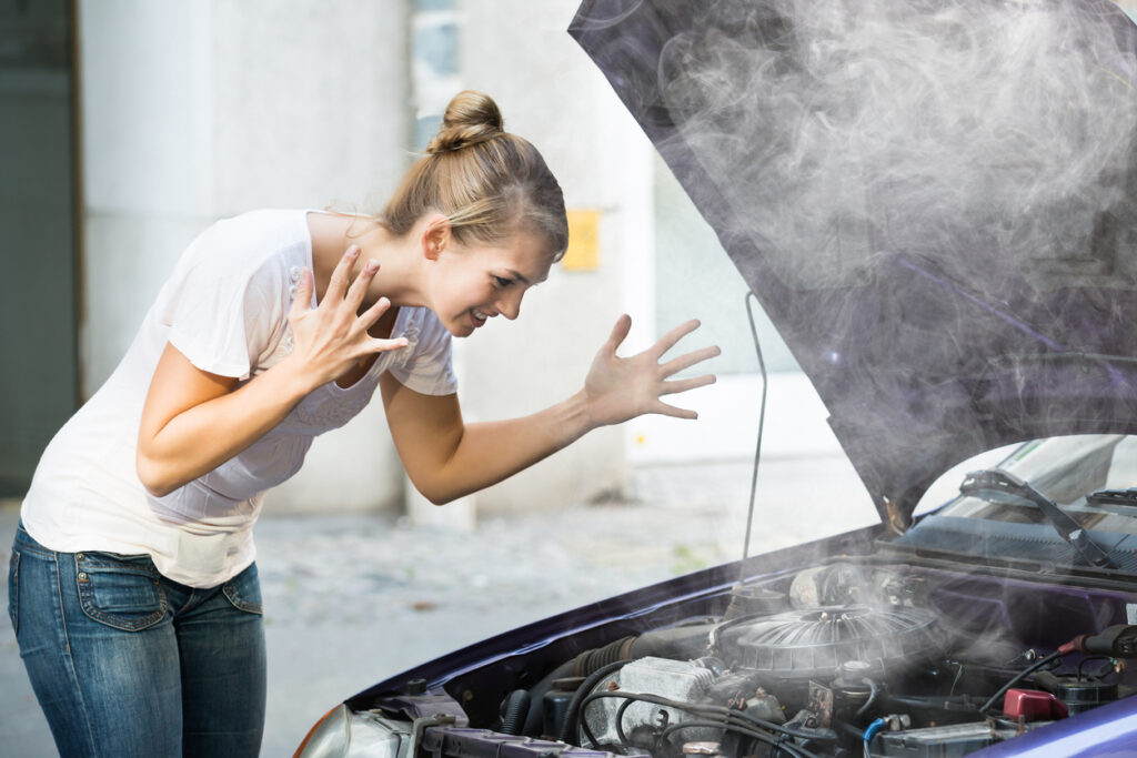 Jeune femme frustrée par la fumée dégageant du capot de sa voiture