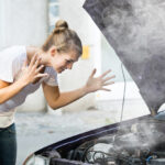 Jeune femme frustrée par la fumée dégageant du capot de sa voiture